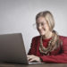Photo of Smiling Woman in a Red Coat and Glasses Using a Laptop
