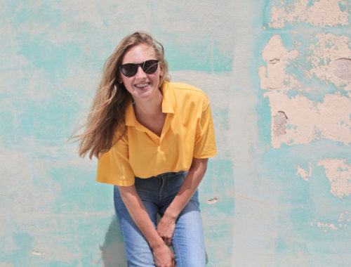 Woman Wearing Yellow Polo Shirt Standing in Front of Teal Concrete Wall Take Care