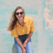 Woman Wearing Yellow Polo Shirt Standing in Front of Teal Concrete Wall Take Care