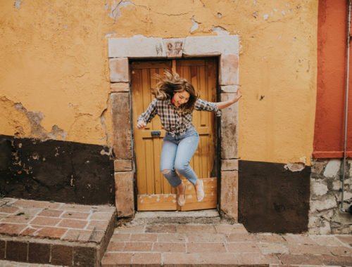 Woman in Black and White Plaid Shirt and Blue Denim Jeans Jumping on Brown Concrete Floor Building a Door