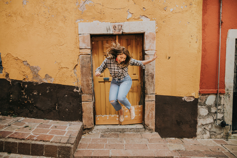 Woman in Black and White Plaid Shirt and Blue Denim Jeans Jumping on Brown Concrete Floor Building a Door